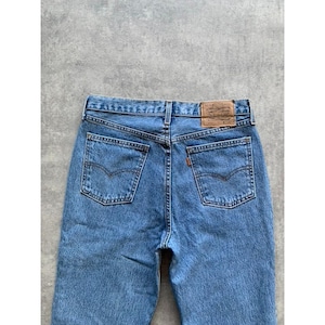 Peut inclure: Jean en denim bleu clair avec une coupe classique à cinq poches. Comprend un patch en cuir marron à la taille et des coutures orange sur les poches arrière. Le jean a une coupe droite.