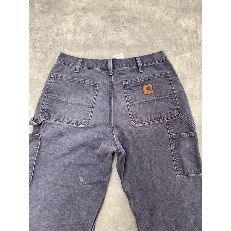 May include: Dark gray work pants with multiple pockets, including a hammer loop and a back pocket with a brown leather patch. The pants are made of a durable fabric and show signs of wear.