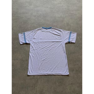 May include: White t-shirt with light blue trim on the collar and sleeves. The shirt is made of a lightweight material and has short sleeves. The shirt is laid flat on a gray surface.