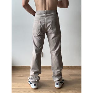 May include: Tan-colored pants with a classic five-pocket design. The pants have a straight leg cut and a neutral color, suitable for various outfits. The back pockets have a unique angular design.