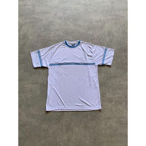May include: White short-sleeve t-shirt with blue and gray stripes across the chest and on the sleeves. The shirt has a blue collar and a small logo on the chest. The shirt is made of a lightweight material.