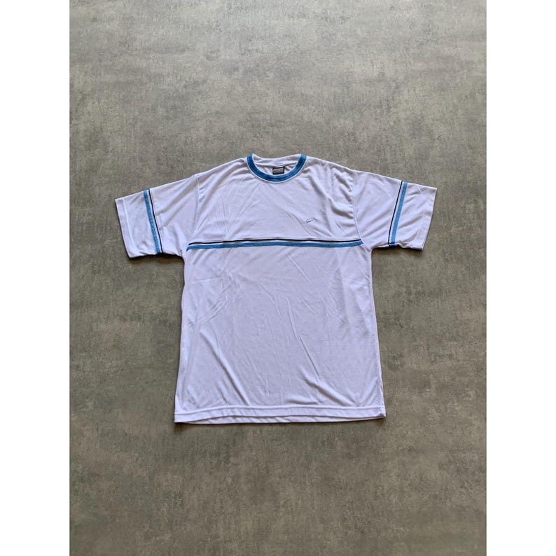 May include: White short-sleeve t-shirt with blue and gray stripes across the chest and on the sleeves. The shirt has a blue collar and a small logo on the chest. The shirt is made of a lightweight material.