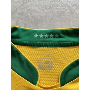 May include: Close-up of a yellow and green athletic jersey. The jersey has a green collar with five white stars. The Nike logo is visible. The jersey has a textured pattern.