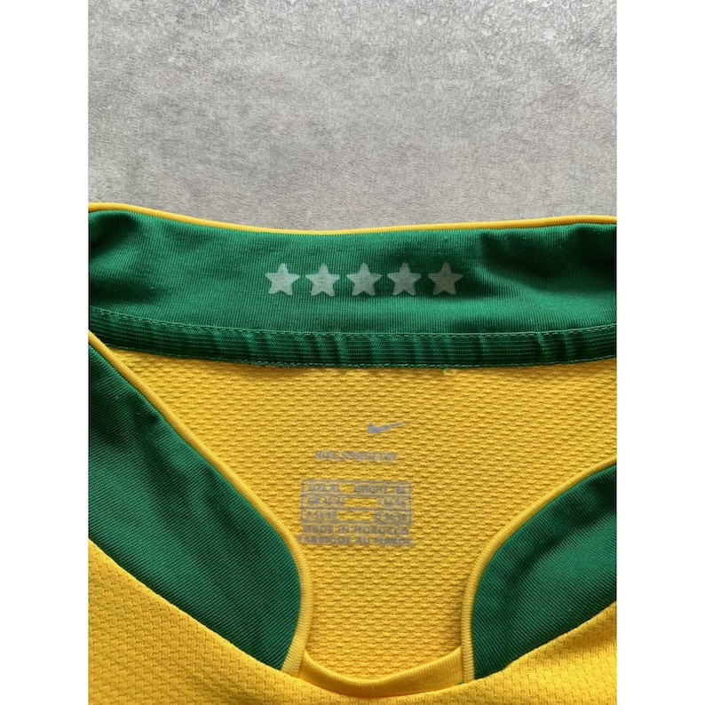 May include: Close-up of a yellow and green athletic jersey. The jersey has a green collar with five white stars. The Nike logo is visible. The jersey has a textured pattern.