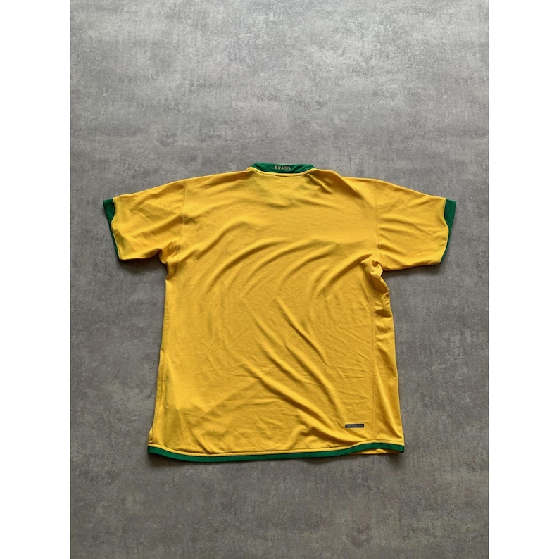 May include: A yellow Brazil soccer jersey with green trim on the collar and sleeves. The word "Brasil" is visible on the back of the collar. The jersey is made of a lightweight material.