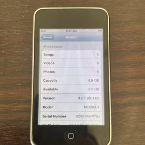 May include: A black iPod digital media player with a silver frame. The screen displays the About menu, showing the device name iPod shahar, 6.8 GB capacity, 6.5 GB available, software version 4.2.1 (8C148), model MC086BT, and serial number 9C001AWP75J.