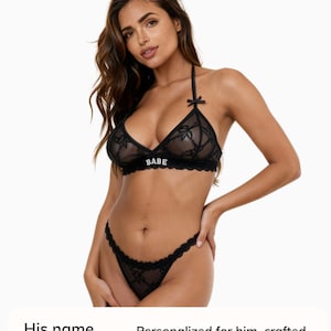 May include: Black lingerie set with a halter-neck bra, the word "BABE", and matching thong. The set is made of a delicate, see-through fabric with floral detailing. The lingerie set is designed for comfort.