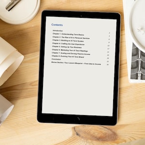 May include: A black tablet displays a document titled "Contents" with a list of chapters about tarot and AI. The tablet is on a light wooden surface, with rolled paper and a white circular object with pins nearby. The text includes chapter titles like "Understanding Tarot Basics."