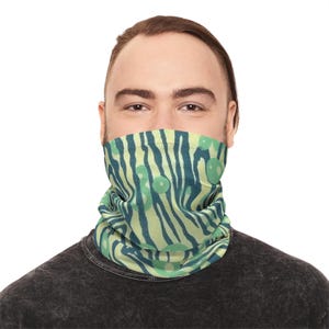 Könnte beinhalten: Ein Halstuch mit einem grün-blauen Zebra-Streifenmuster und kreisförmigen Akzenten. Das Halstuch wird um den Hals getragen und bedeckt das untere Gesicht. Die Person auf dem Bild trägt ein dunkelgraues T-Shirt.