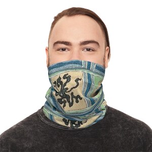 Könnte beinhalten: Ein Halstuch mit einem einzigartigen Design. Das Halstuch zeigt ein beiges Quadrat mit einem schwarzen floralen Muster, umgeben von blauen und grünen Streifen. Die Person auf dem Bild trägt ein dunkelgraues T-Shirt.