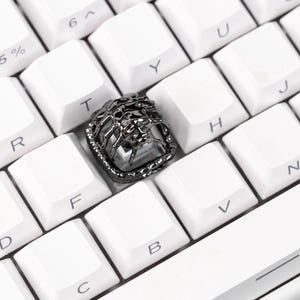 May include: Close-up of a white mechanical keyboard with a custom keycap. The keycap is dark gray with a detailed design, possibly a lion's head. The keyboard has a purple accent.