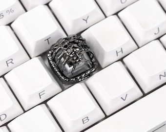 Pode incluir: Close-up de um teclado mecânico branco com uma tecla personalizada. A tecla é cinza escuro com um design detalhado, possivelmente uma cabeça de leão. O teclado tem um detalhe roxo.