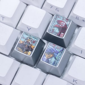 May include: A close-up of a white mechanical keyboard with custom keycaps. The keycaps feature colourful anime-style artwork and Japanese text. The keyboard has a purple accent and is lit with a soft glow.
