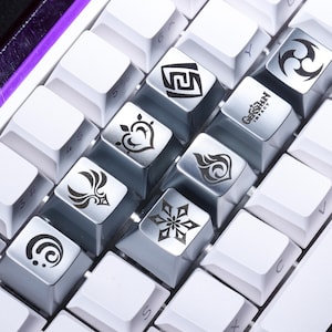 Op de afbeelding: Een close-up van een wit mechanisch toetsenbord met aangepaste keycaps. De keycaps hebben verschillende symbolen en het "Genshin Impact" logo. Het toetsenbord heeft een paarse accentkleur aan de zijkant.