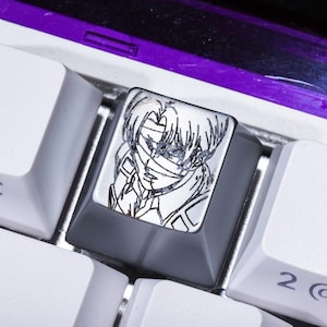 May include: A custom keyboard keycap with a black and white anime-style illustration of a character with a bandage over their eyes. The keycap is grey and surrounded by white keyboard keys.
