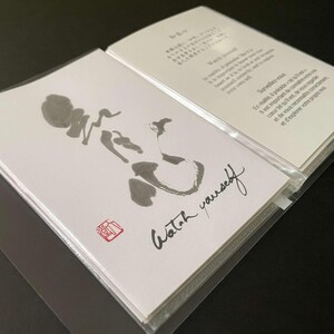 May include: Two white cards in plastic sleeves. One card features a black ink drawing and the words "Watch yourself" in cursive. The other card has text in multiple languages. A red stamp is in the corner.