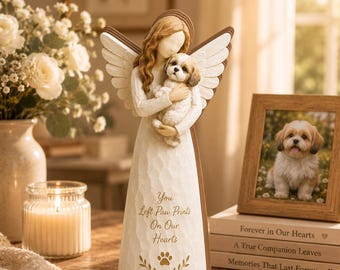 May include: A white angel figurine holding a small dog, with text that reads "You Left Paw Prints On Our Hearts." A framed photo of a dog and stacked books are also present. The angel has brown hair and wings.