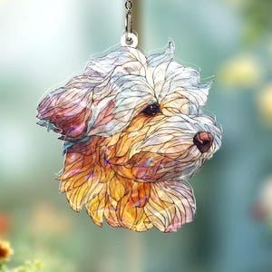 May include: A decorative dog-shaped ornament, suspended by a chain. The ornament features a watercolor-style design with a white and gold coat, pink accents, and dark eyes. The dog's head is turned to the side.