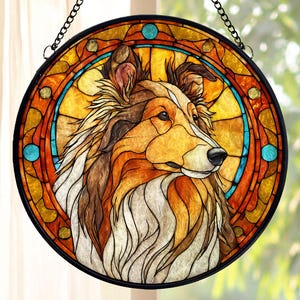 May include: A round stained glass window featuring a dog's profile. The artwork uses shades of brown, orange, yellow, and white, with blue accents. The window is framed in black and hangs from a chain.