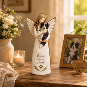May include: A carved angel figurine holding a black and white dog. The angel wears a white dress and has feathered wings. The text "Forever in Our Hearts" is on the dress. A framed photo and a heart-shaped plaque are also visible.