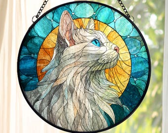 May include: Round stained glass window art featuring a cat with blue eyes, set against a yellow and blue background. The cat is depicted in shades of white and gray, with a black metal frame and chain for hanging.