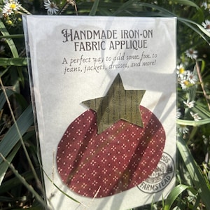 May include: A handmade iron-on fabric applique in the shape of a red oval with a small white dot pattern and a green star with a dark vertical line pattern. The applique is packaged in a clear plastic sleeve with text reading HANDMADE IRON-ON FABRIC APPLIQUE.