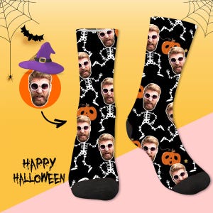 May include: Black Halloween socks featuring a repeating pattern of a person's face, skeleton illustrations, and orange pumpkins. The socks have black heels and toes. The words "Happy Halloween" are visible in the image.