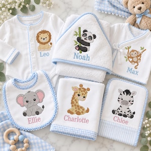 May include: A collection of white baby items including a long-sleeve bodysuit with a lion, a hooded towel with a panda, a wrap shirt with a monkey, a bib with an elephant, and two washcloths with a giraffe and zebra, all featuring embroidered names.