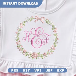 May include: A white baby bib featuring a central pink embroidered monogram of the letters H and F enclosed within a circular floral wreath of pink roses, small white flowers, and green leaves, topped with a small pink bow.