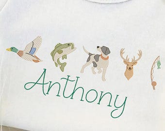May include: White baby onesie with embroidered illustrations of a duck, fish, dog, deer, and fishing rod. The name "Anthony" is embroidered in green script below the images. A cute and personalized baby gift.