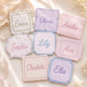 Peut inclure: Un ensemble de huit dessous de verre en tissu carrés et rectangulaires avec des prénoms brodés : Emma, Olivia, Amelia, Sophia, Lily, Ava, Charlotte et Ella. Les dessous de verre présentent divers motifs pastel comme le vichy et des fleurs.