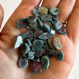 May include: A collection of teal and grey tumbled gemstones, each with striking pink and red inclusions. The stones are of various sizes and shapes, displaying natural textures. Suitable for jewellery making or collecting.