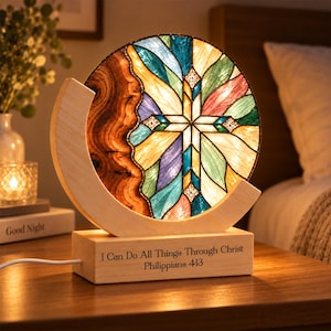 Könnte beinhalten: Eine kreisförmige Lampe mit einem Buntglas-Kreuzdesign in blauen, grünen, violetten und gelben Feldern. Das Glas ist von einer natürlichen Holzhalbmondform und einem rechteckigen Sockel mit der Gravur I Can Do All Things Through Christ Philippians 4:13 umrahmt.