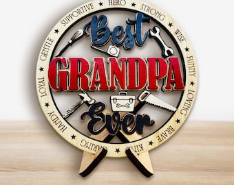 Peut inclure: Panneau en bois "Best Grandpa Ever". Les mots sont en bleu, rouge et noir, avec des outils et des mots positifs autour du bord. Le panneau est soutenu par un support en bois.