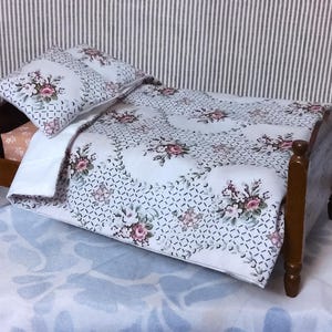 May include: A miniature wooden bed with floral bedding. The bed frame is a dark brown color. The bedding includes a pillow and a quilt with a white background and pink and green floral pattern. The bed is on a light blue surface.