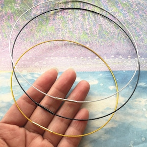May include: Three necklaces in gold, silver and black. The necklaces are made of thin, braided wire and are lying on a hand.