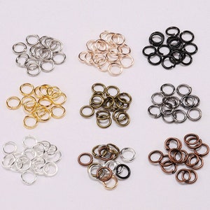 May include: A selection of jump rings in different metallic colours, such as silver, gold, bronze, and black. These small, circular rings are used for jewellery making and crafts. The jump rings are arranged in small piles.