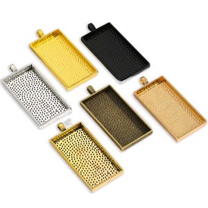 Könnte beinhalten: Sechs rechteckige Anhänger-Tabletts in Gold-, Silber-, Schwarz- und Bronzetönen. Jedes Tablett hat eine strukturierte Oberfläche und eine Schlaufe oben zum Befestigen an einer Kette oder einem Band. Ideal für die Schmuckherstellung.