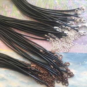 May include: A close-up of a large bundle of black leather cords with silver and copper clasps. The cords are arranged in a neat pile, with the clasps visible at the ends.