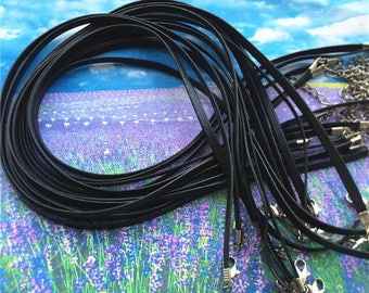 Puede incluir: Un conjunto de collares de cordón de satén negro con cierres de langosta plateados. Los cordones están dispuestos en forma circular, con los cierres visibles en la parte inferior.