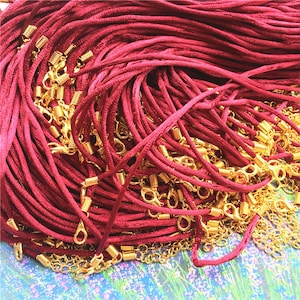 May include: A pile of burgundy-colored necklace cords with gold-colored clasps and chain extenders. The cords are tightly bundled together, with the gold accents creating a contrast against the deep red. The image suggests jewelry-making supplies.