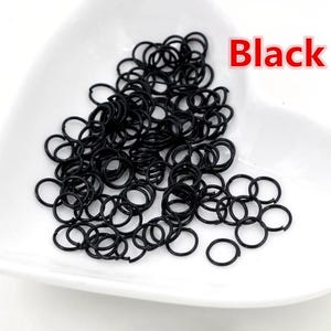 May include: A large quantity of small, black metal jump rings. The rings are all the same size and are arranged in a pile.