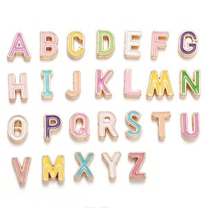 Peut inclure: Un ensemble de breloques de lettres de l'alphabet colorées. Chaque lettre est bordée d'or et remplie d'une couleur pastel différente, notamment rose, jaune, vert et bleu. Les lettres sont disposées en rangées, présentant tout l'alphabet.