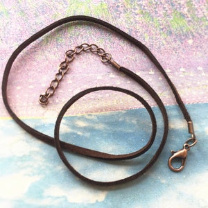 Puede incluir: Un collar de cordón de cuero marrón con una cadena y un cierre de bronce.