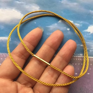 May include: A gold-colored necklace with a twisted rope design. The necklace is held together by a small, gold-colored clasp. The necklace is a simple, elegant piece of jewelry.