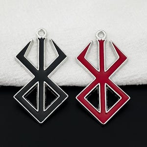 May include: Two metal pendants with a geometric design. One pendant is black with a silver border, and the other is red with a silver border. Both have a loop at the top for attaching to a chain or cord. The pendants are likely for jewelry making.
