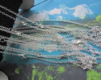 May include: A close-up of a pile of silver chain necklaces with lobster claw clasps. The chains are arranged in a layered pattern, with some chains overlapping others.