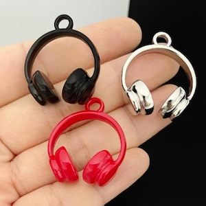 Könnte beinhalten: Drei Miniatur-Kopfhörer-Anhänger in Schwarz, Silber und Rot. Jeder Anhänger hat einen kreisförmigen Bügel mit zwei Ohrmuschel-Details und einer kleinen Schlaufe zum Befestigen an Schmuck oder anderen Bastelarbeiten. Die Anhänger werden vor einem neutralen Hintergrund gezeigt.