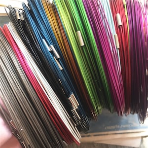 Puede incluir: Una variedad de cordones coloridos con terminales plateados. Los cordones están dispuestos en forma de abanico, con los terminales plateados visibles en la parte superior de la imagen.