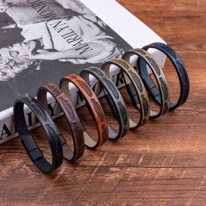 May include: Seven leather bracelets with feather patterns in a range of colours, including black, brown, grey, and blue. Each bracelet features a magnetic clasp. The bracelets are presented on a wooden surface.